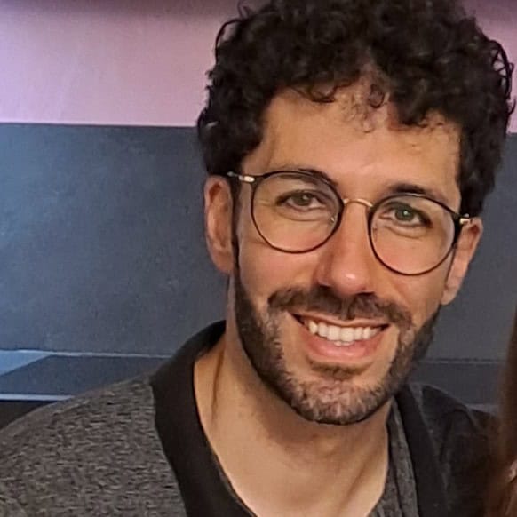 Uomo sorridente con occhiali, sfondo scuro, immagine professionale.