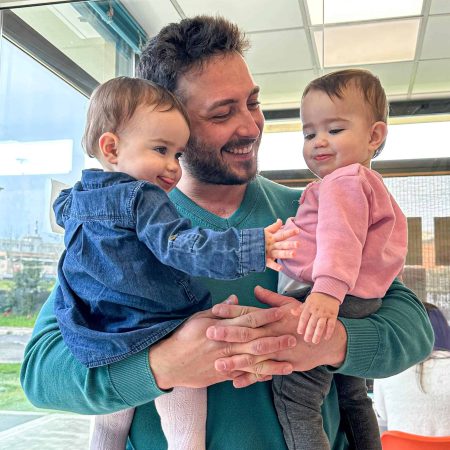 Padre con due bambine sorridenti in un ambiente luminoso e moderno.